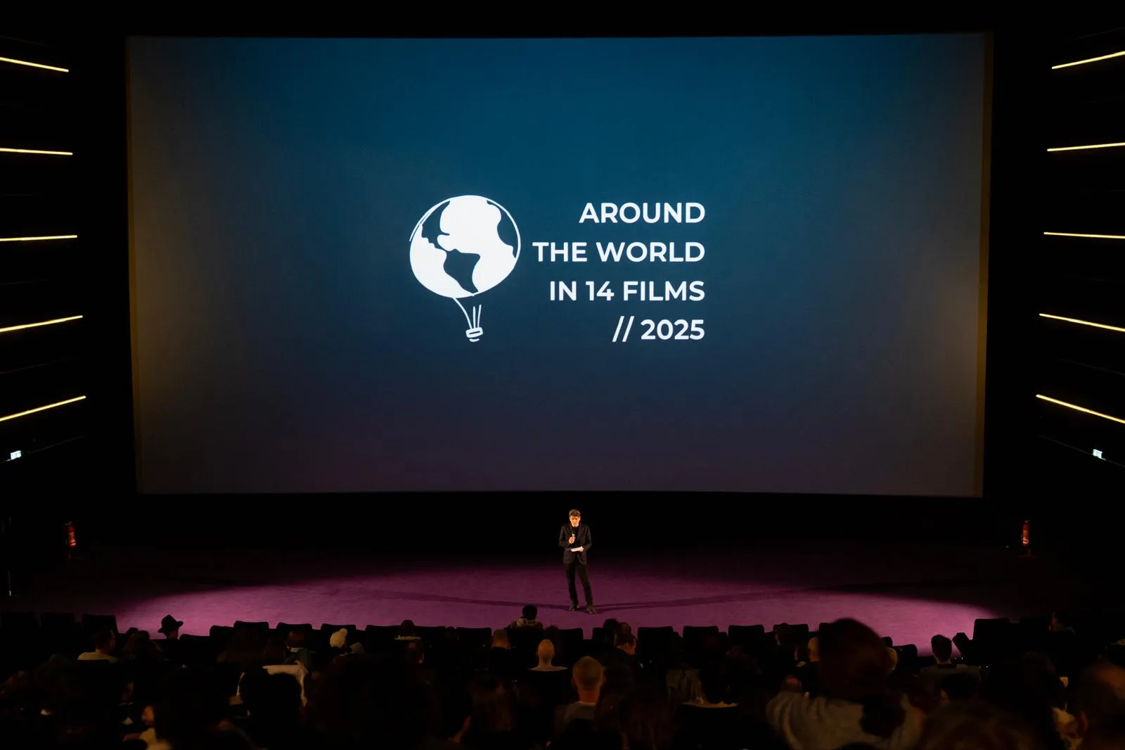 Volles Haus, auf der Leinwand das Festivallogo mit der Jahreszahl 2025, davor spricht eine Person auf der Bühne